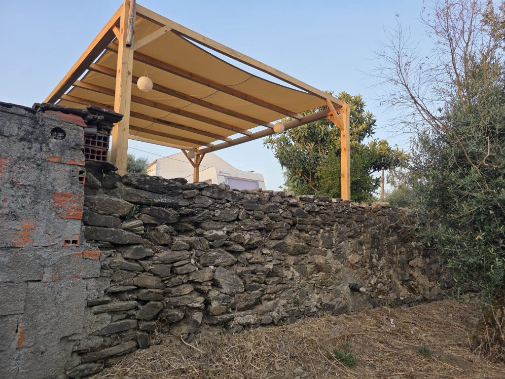 Construção de pérgola em madeira sobre pátio com piso de pedra.